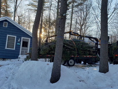 A truck is carrying a christmas tree to a house in the snow.