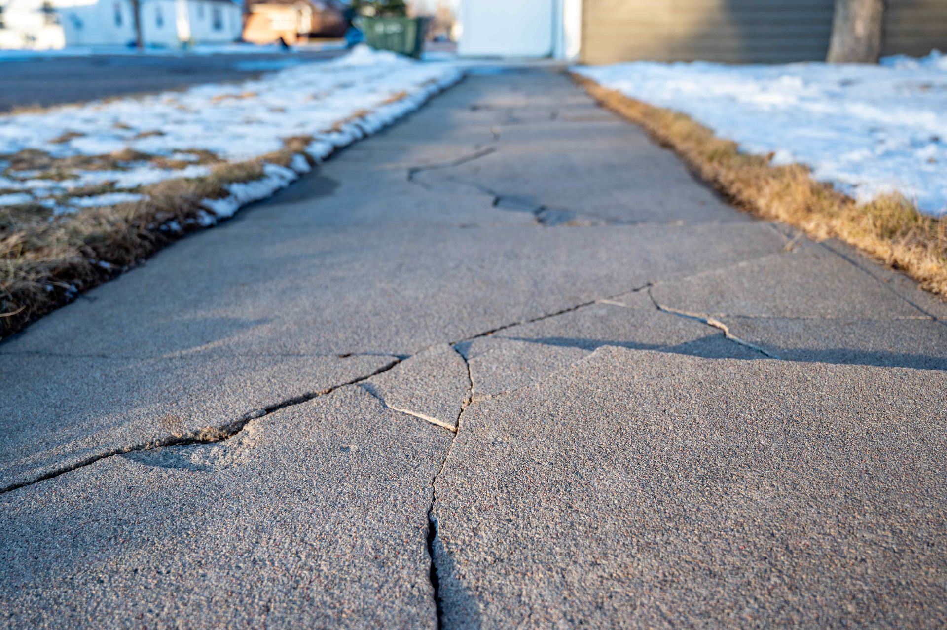 Cracked concrete sidewalk with snow on the edges in a residential setting.