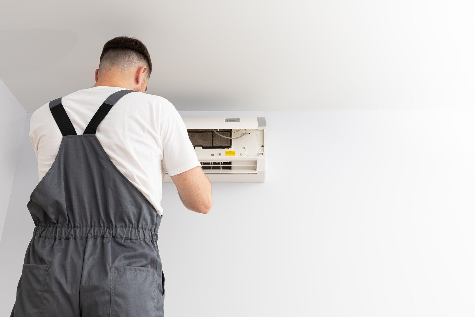 A man in overalls is installing an air conditioner on a wall.