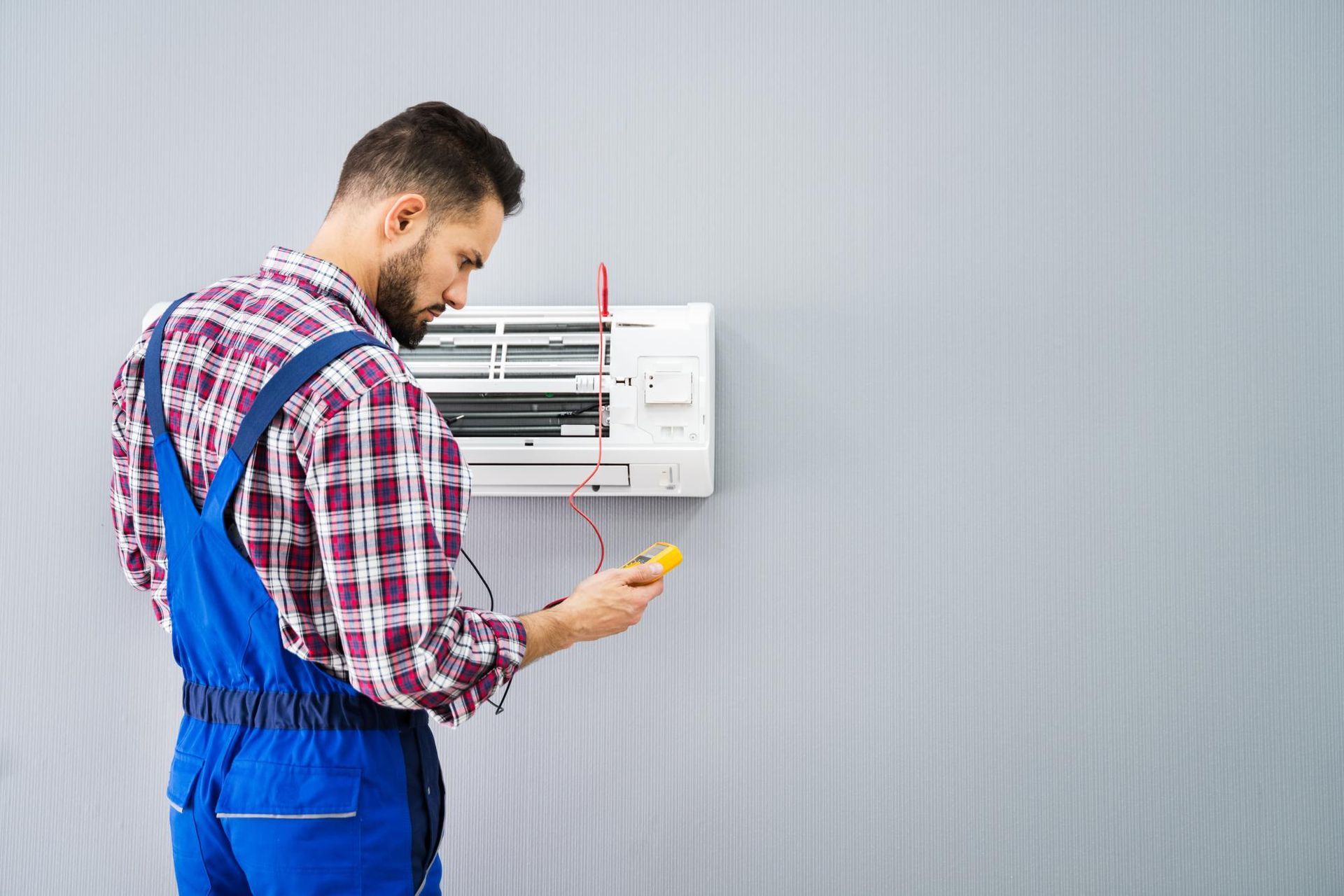 A man is fixing an air conditioner with a screwdriver.