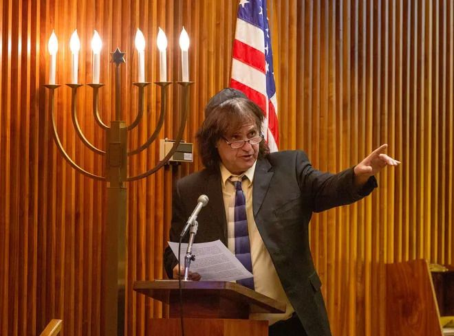 A man in a suit and tie is giving a speech in front of a menorah