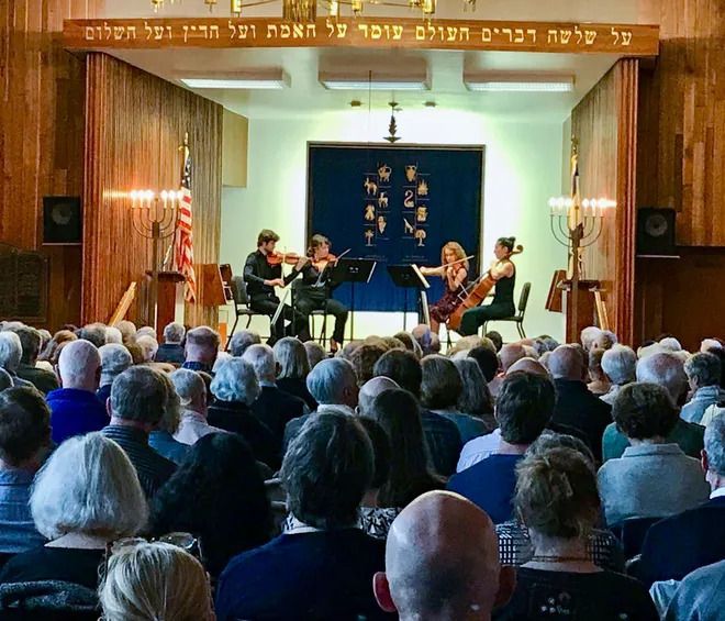 A large group of people are sitting in a room watching a concert.