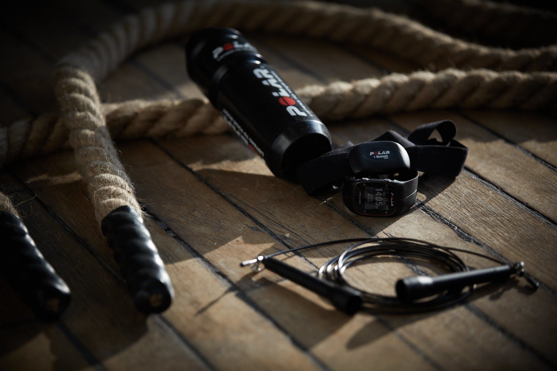 Een touw, een springtouw en een slim horloge liggen op een houten tafel.
