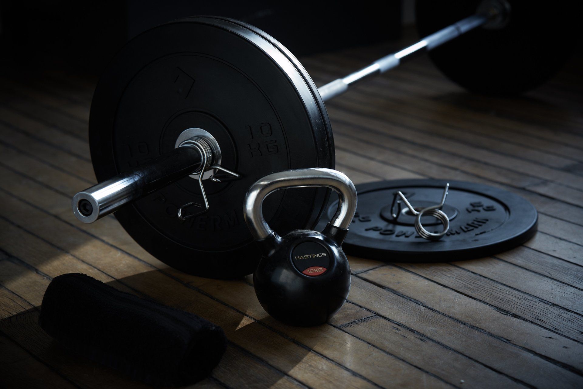Een halter en een kettlebell liggen op een houten vloer