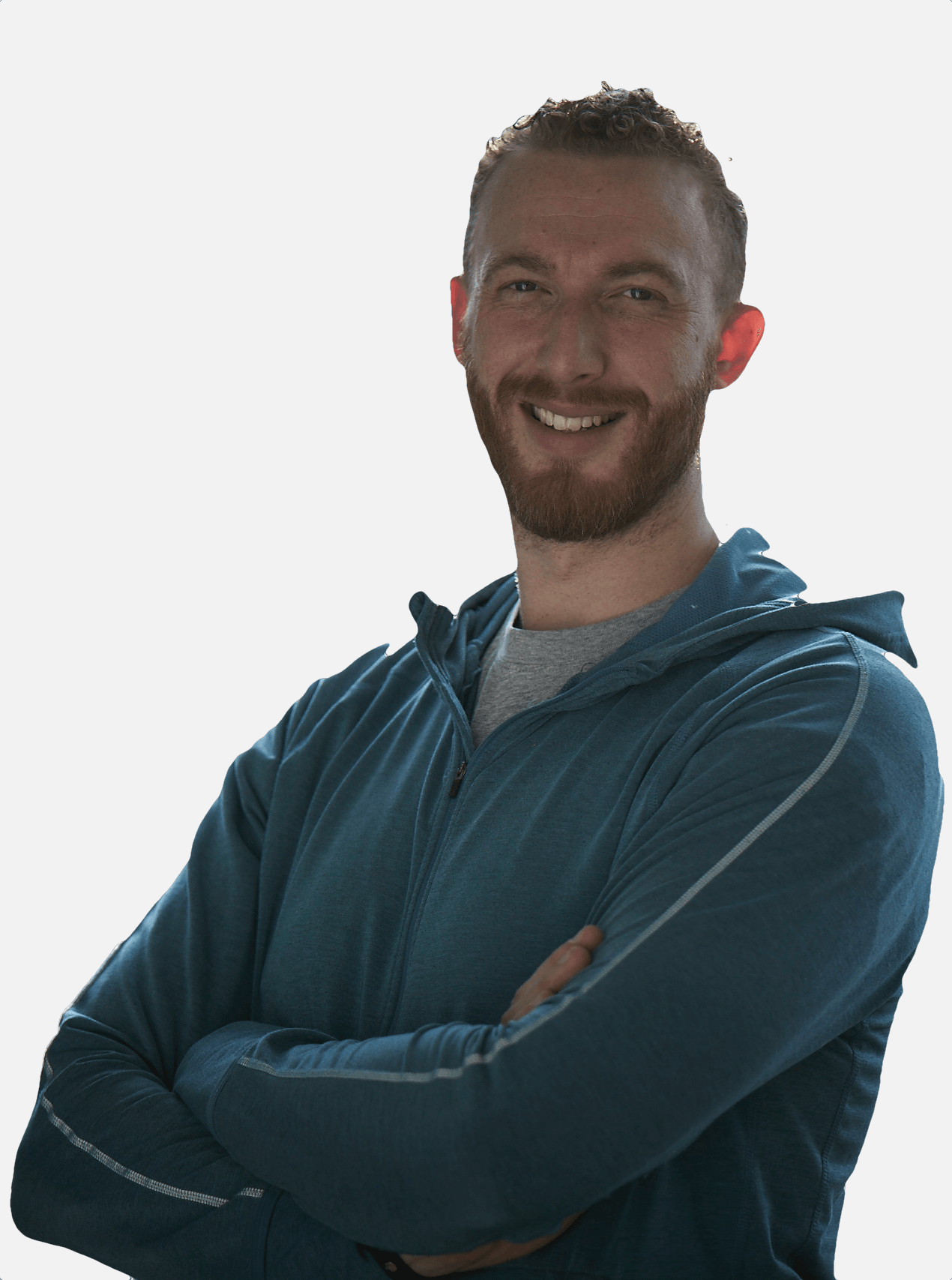 Een man met een baard staat met zijn armen over elkaar en lacht.