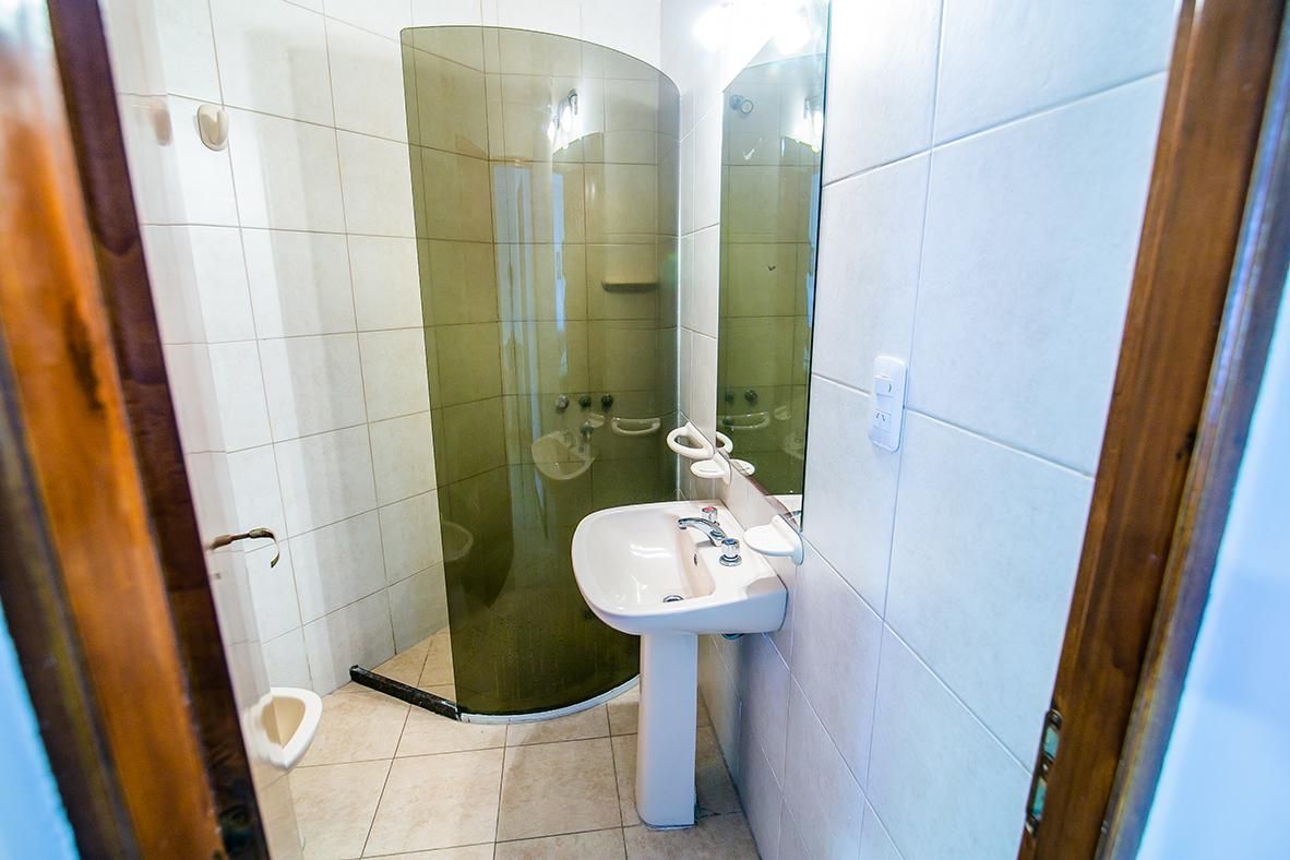 Baño pequeño con ducha de cristal, lavabo con pedestal y paredes alicatadas en azul.
