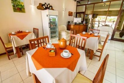 Acogedor comedor de restaurante con mesas blancas, manteles naranjas, sillas de madera y vistas a la cocina.
