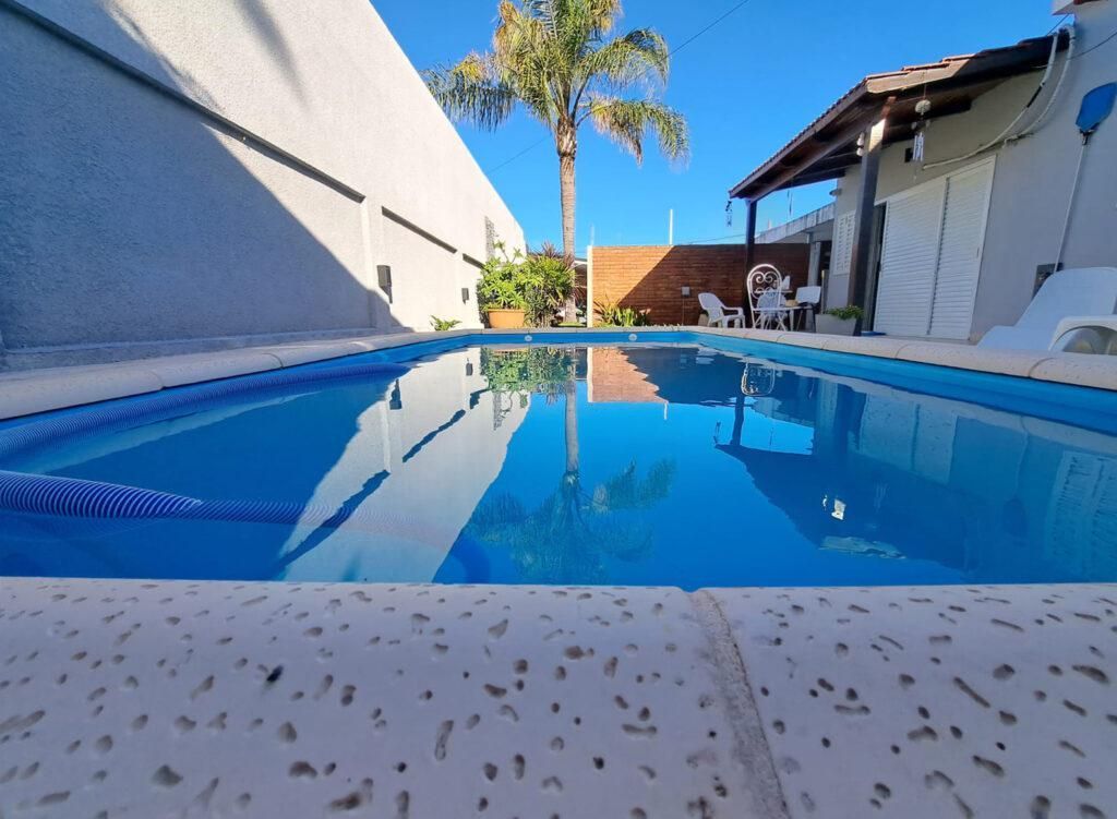 Piscina en el patio trasero con agua azul, paredes blancas y palmeras que se reflejan en la superficie.