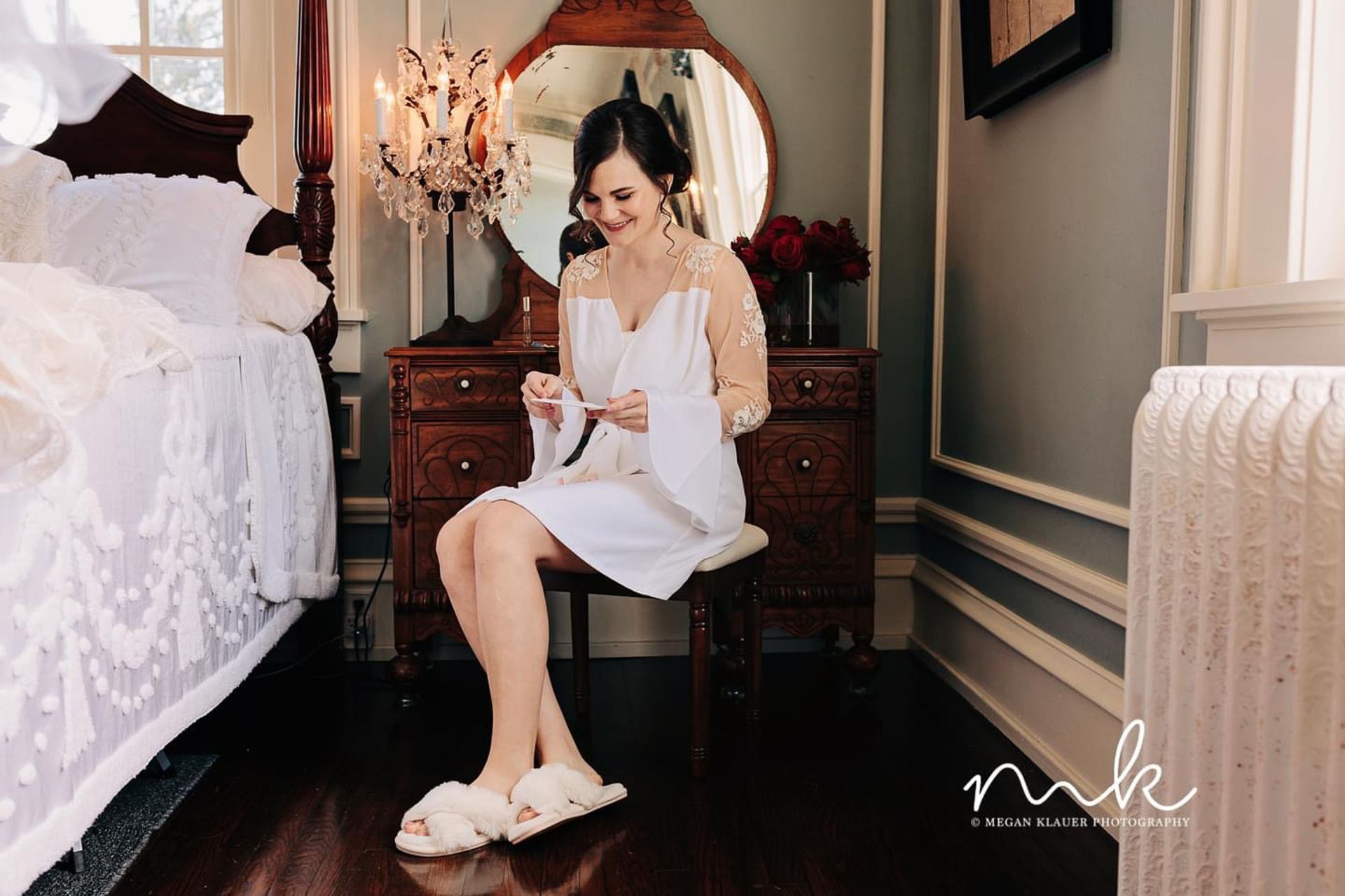 A woman is sitting on a stool in front of a mirror in a bedroom.