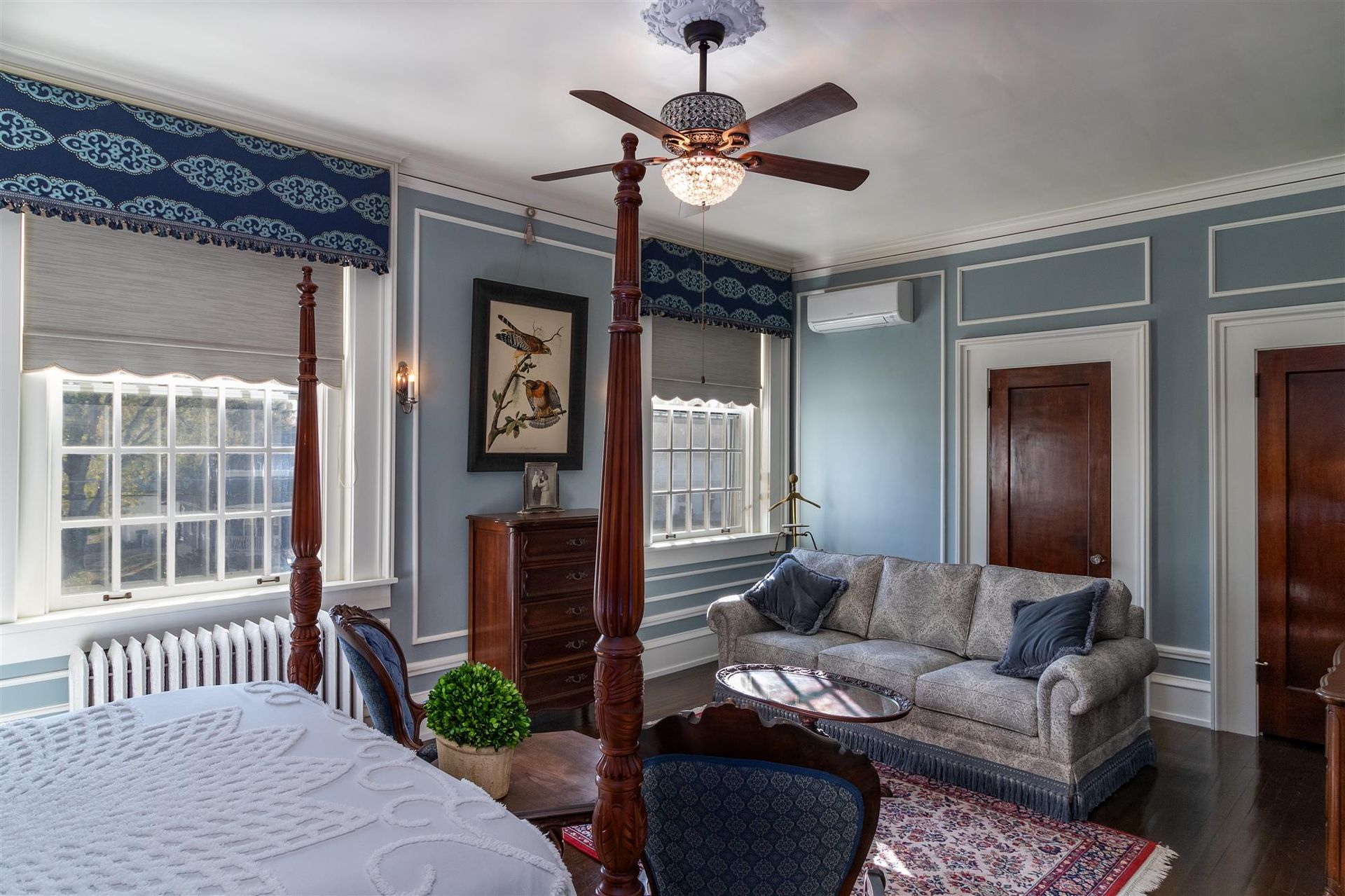 A bedroom with a four poster bed , a couch , and a ceiling fan.
