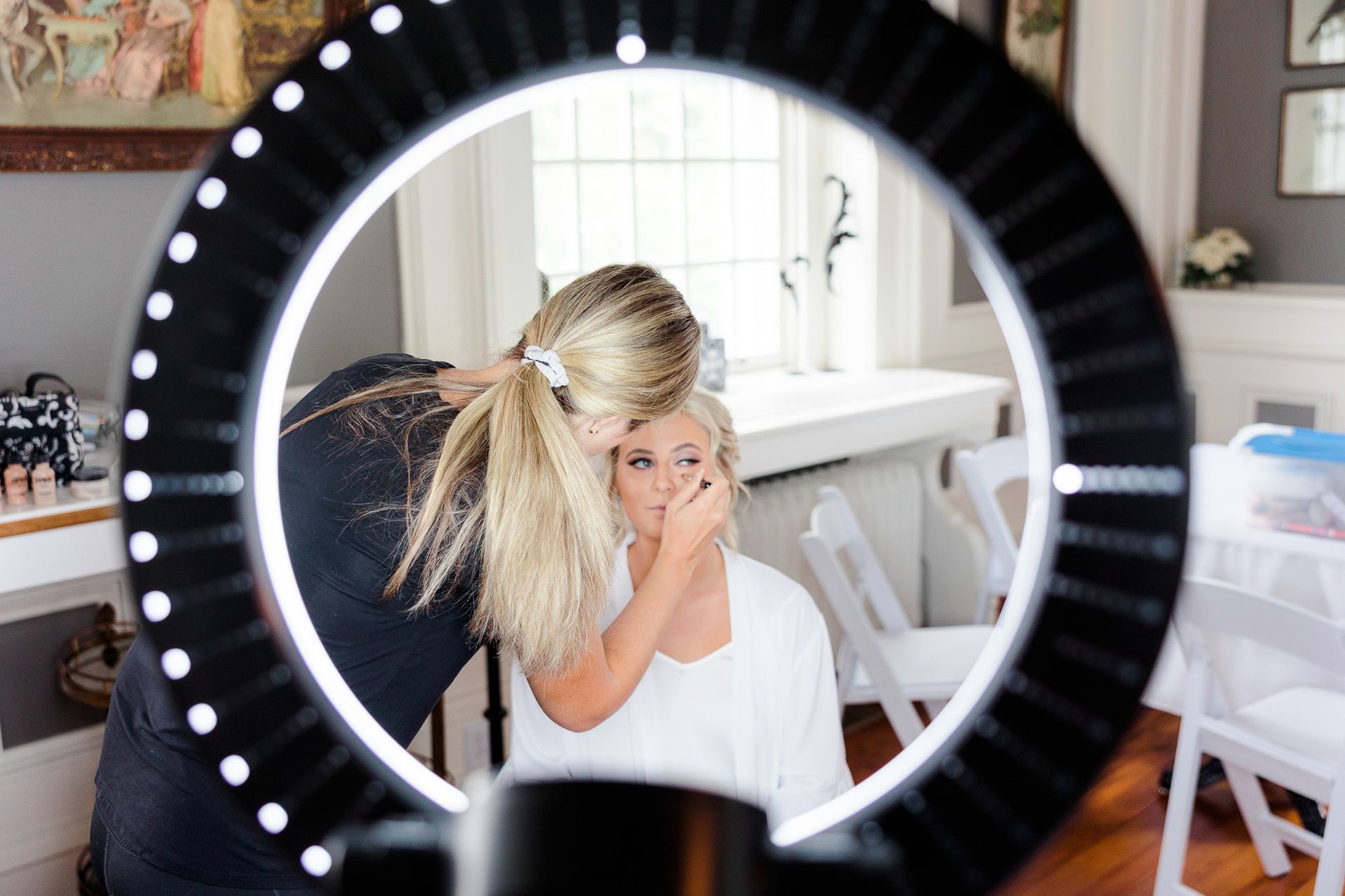 A woman is getting her makeup done in front of a ring light.