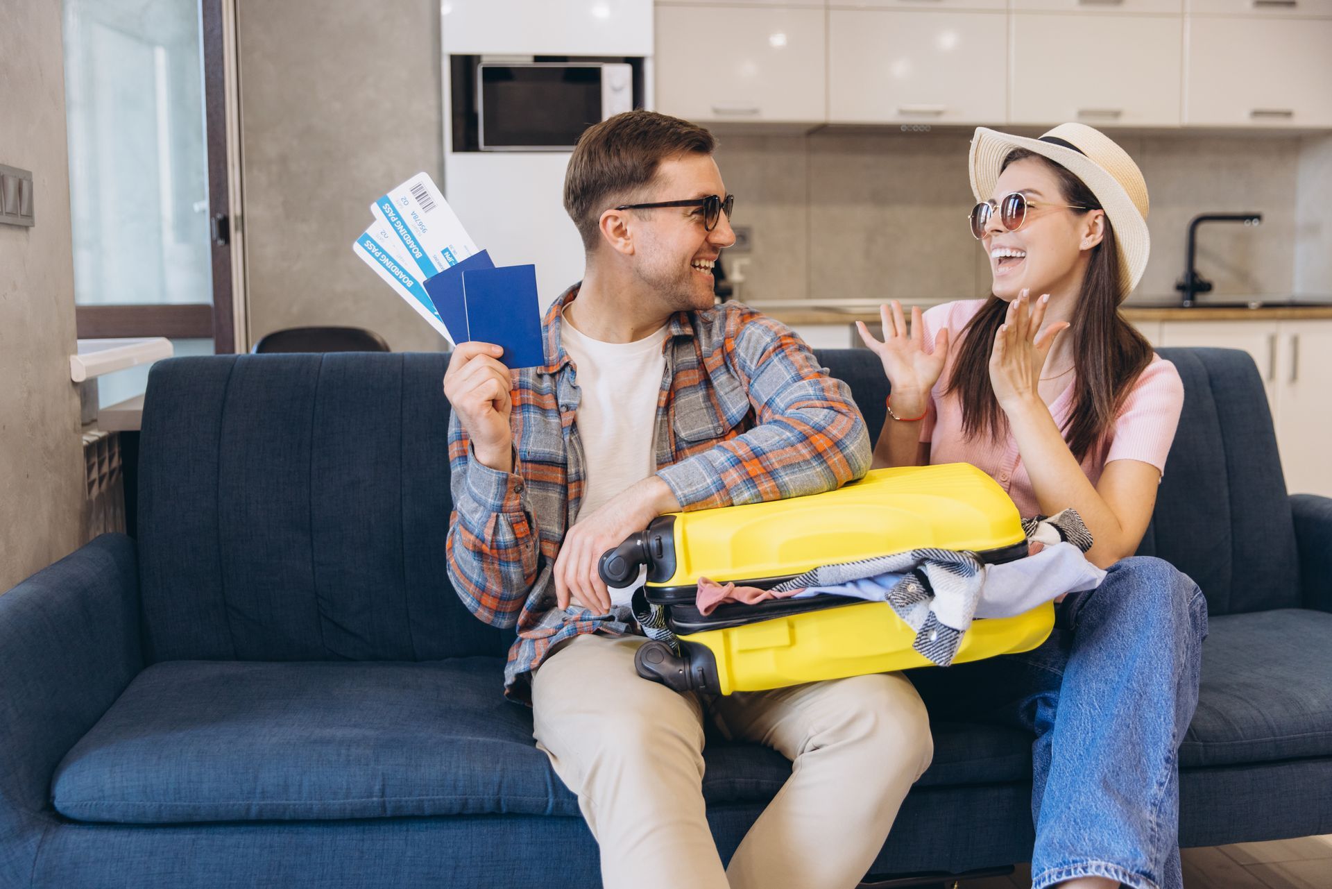 A man and a woman are sitting on a couch with a suitcase and tickets.