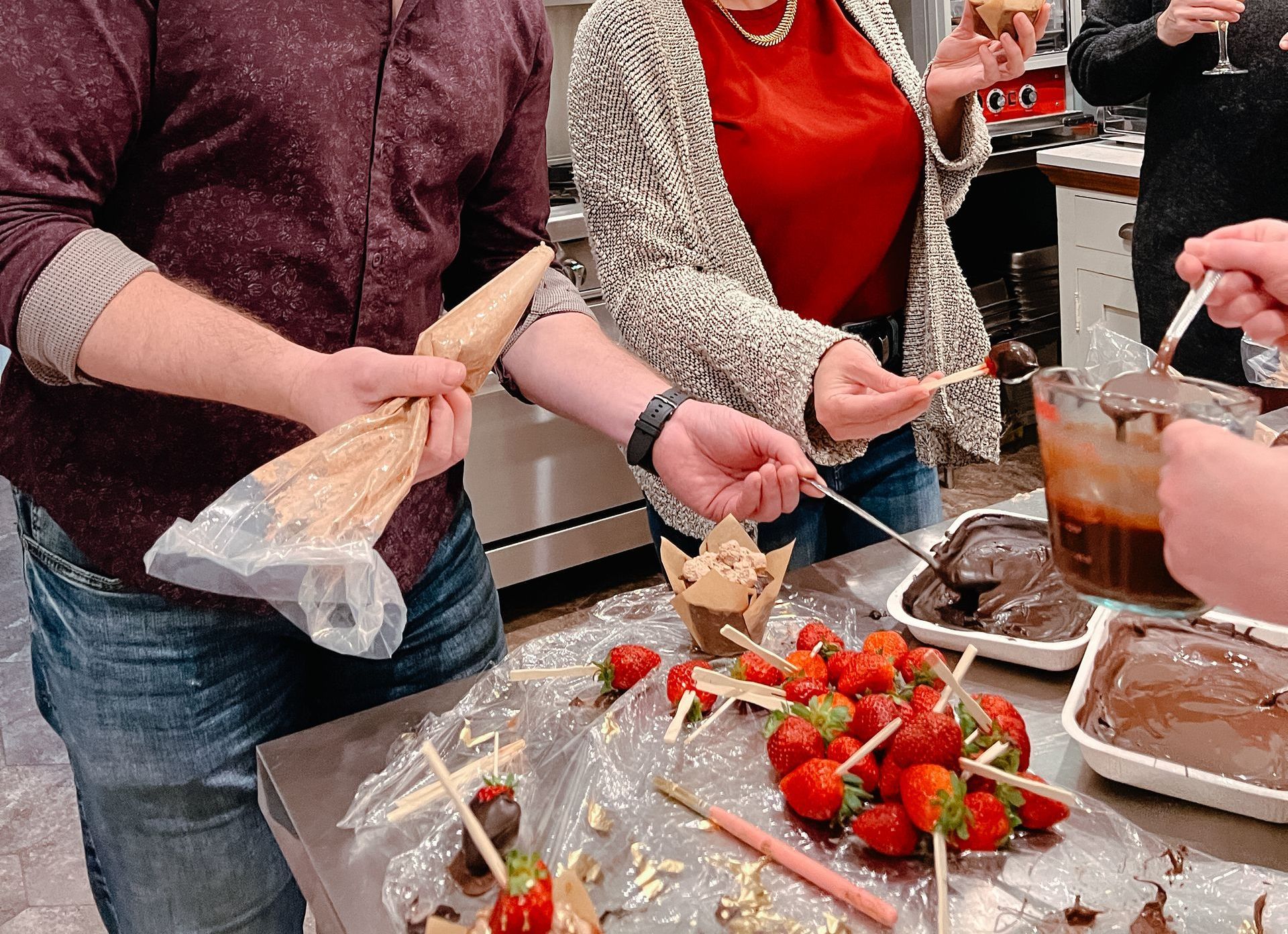A group of people are standing around a table with strawberries and chocolate.