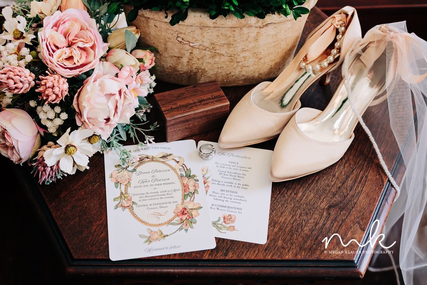 A pair of wedding shoes , a wedding invitation , and a bouquet of flowers are on a wooden table.