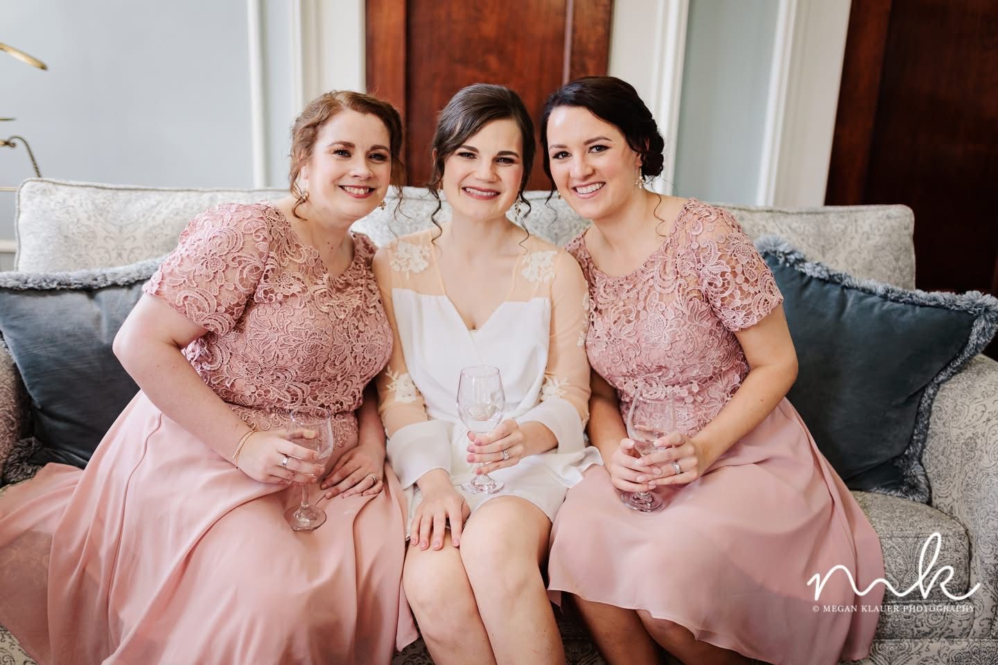 A bride and her bridesmaids are posing for a picture while sitting on a couch.