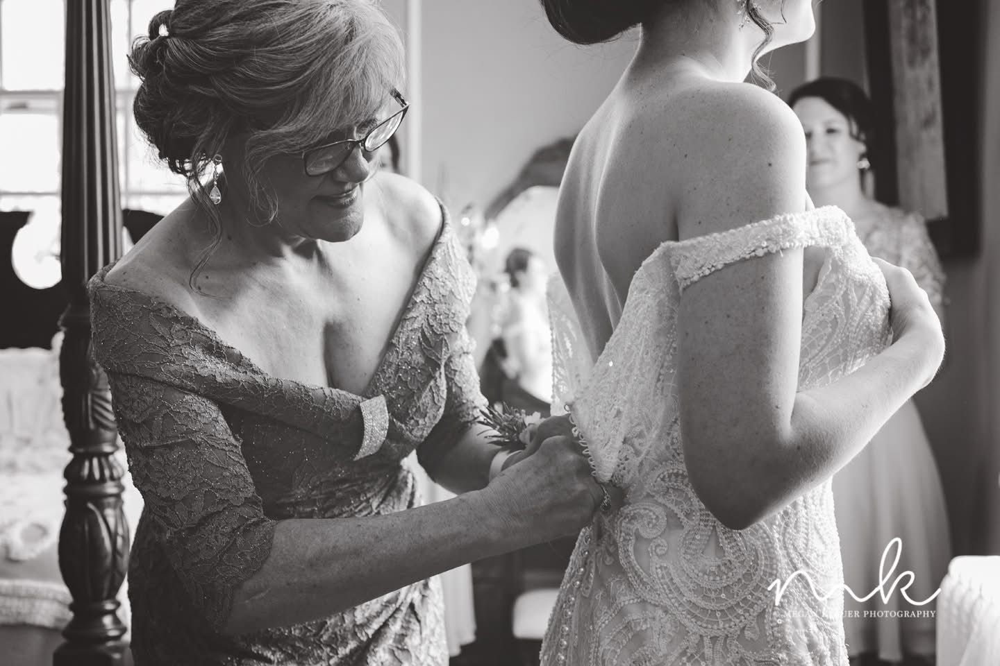A woman is helping a bride get ready for her wedding in a black and white photo.