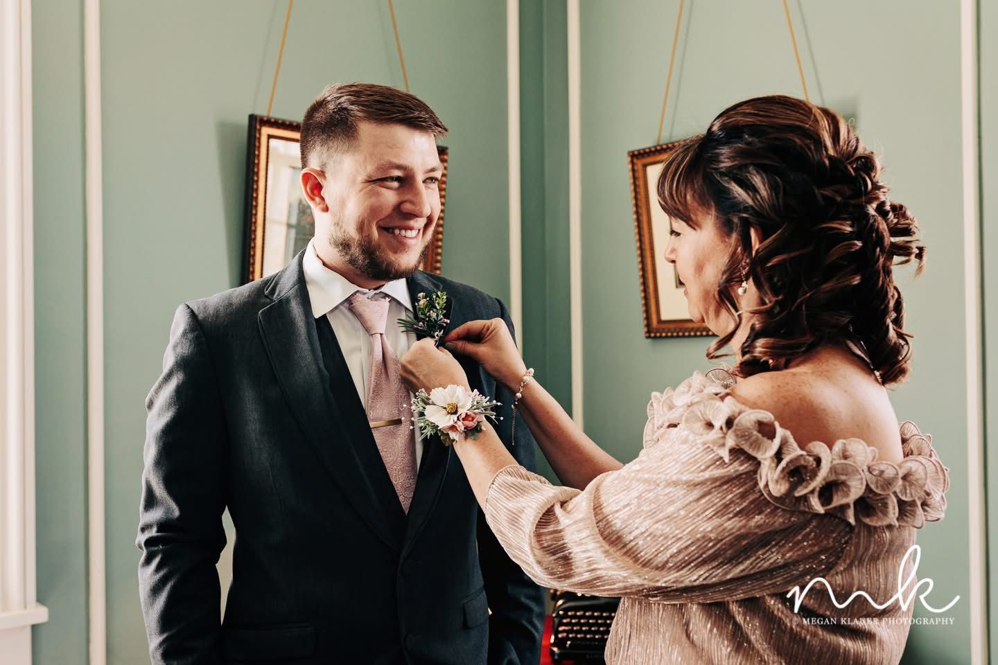 A woman is fixing a buttonhole on a groom 's suit.
