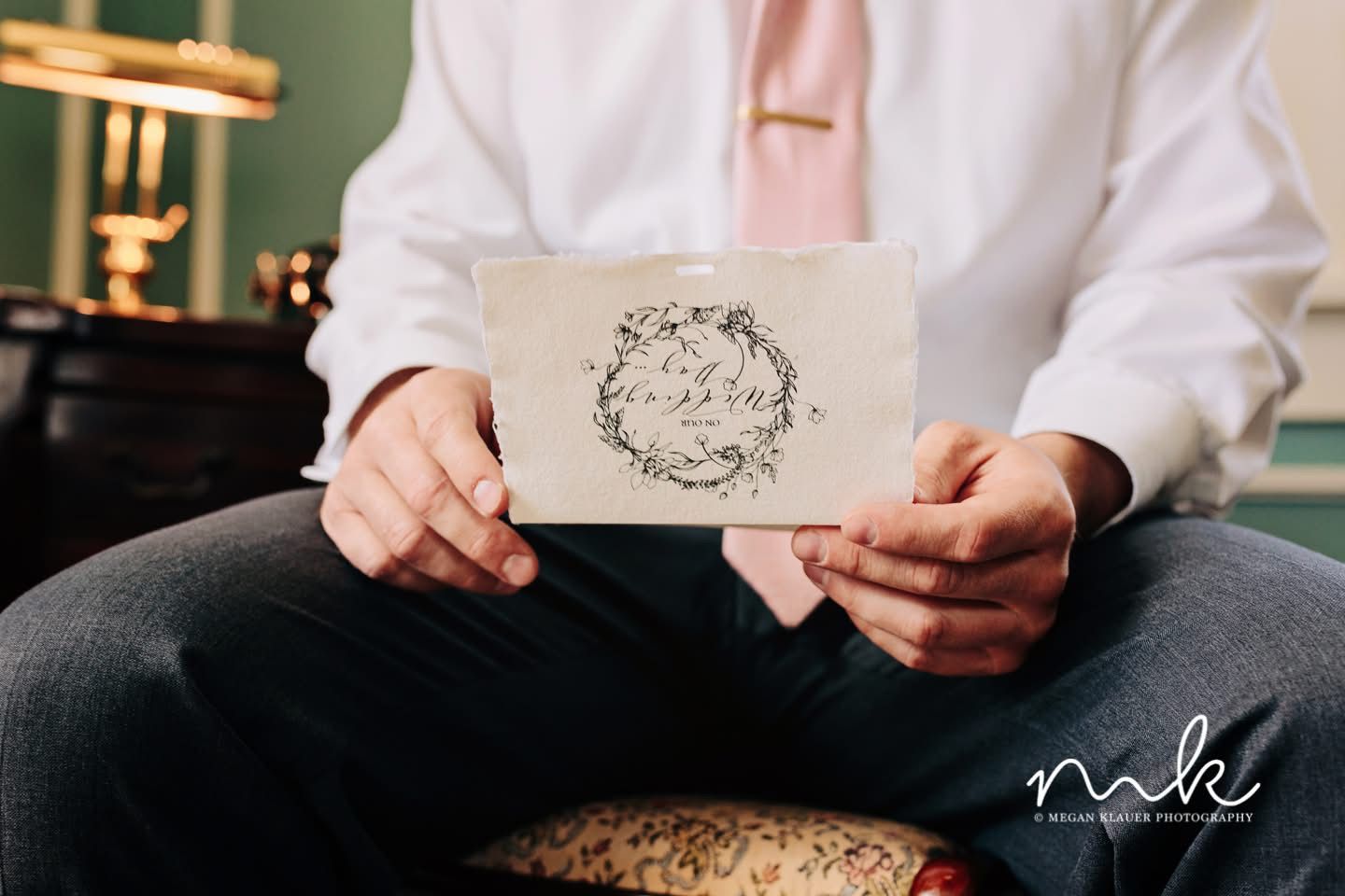 A man in a white shirt and pink tie is holding a card