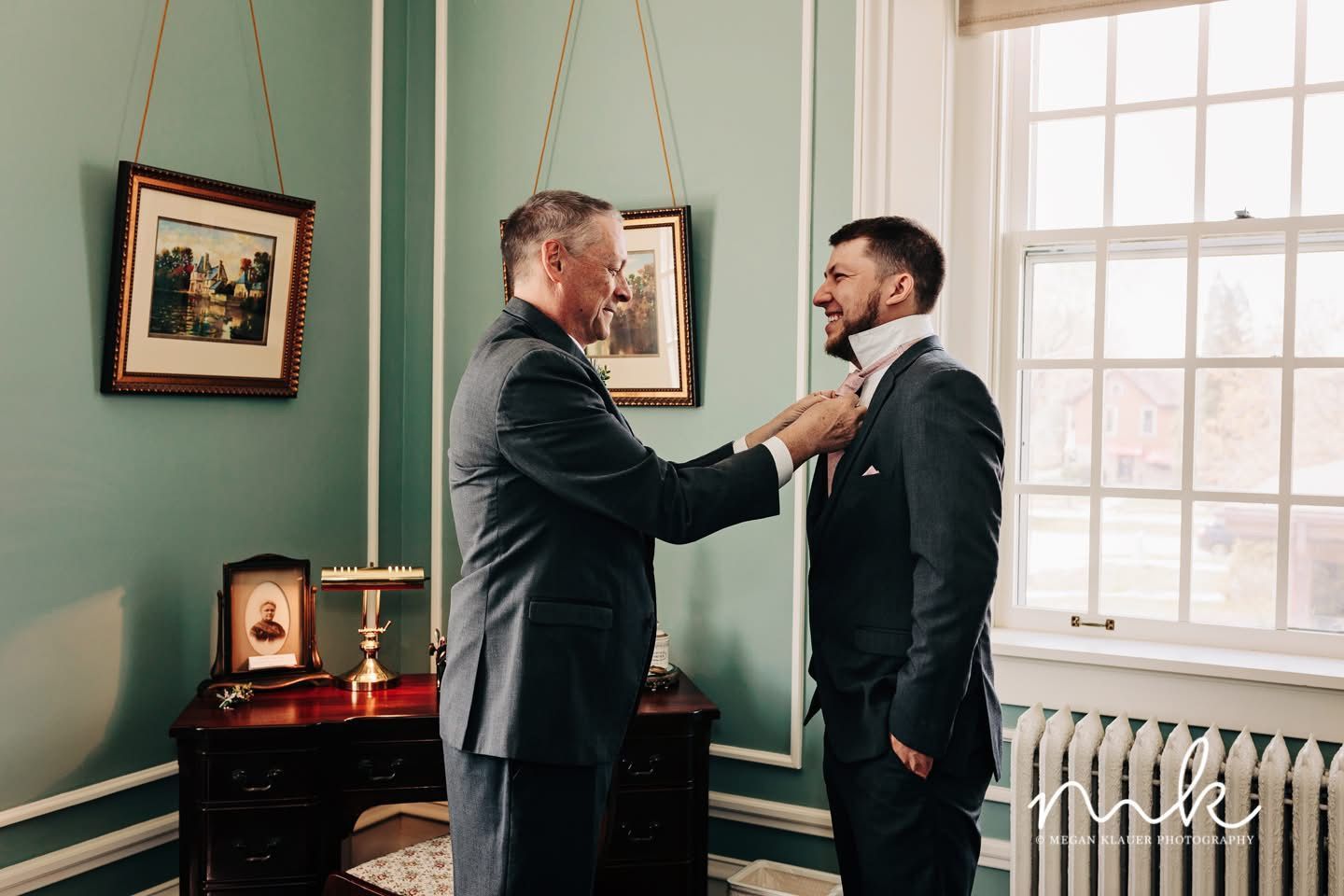 A man is helping another man with his tie in a room.