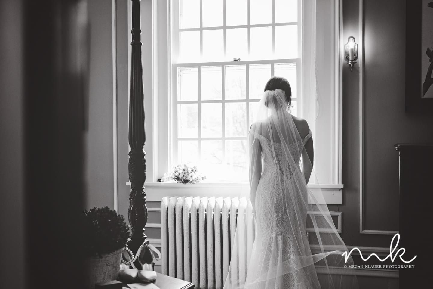 A bride in a wedding dress and veil is standing in front of a window.