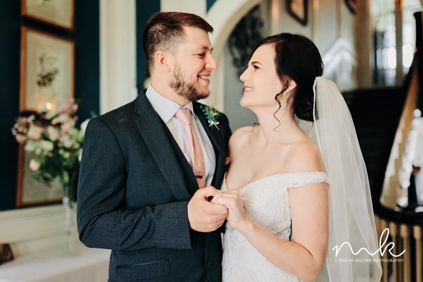A bride and groom are holding hands and smiling at each other.
