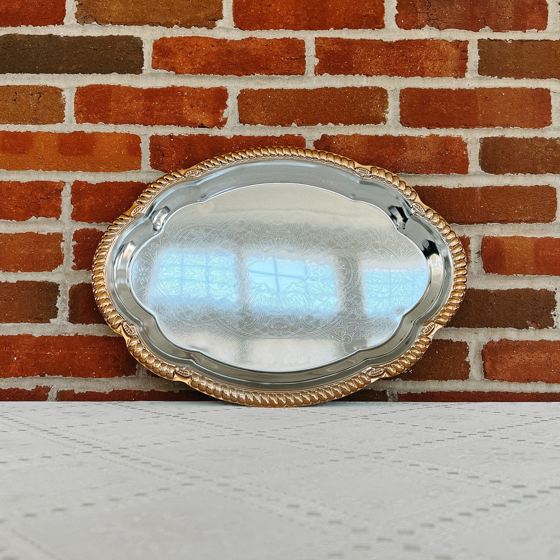 A silver oval tray with a gold rim sits on a table
