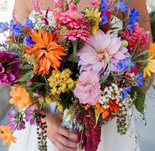 A woman in a white dress is holding a bouquet of colorful flowers