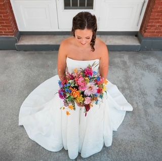 A bride in a white dress is sitting on the steps of a building holding a bouquet of flowers.