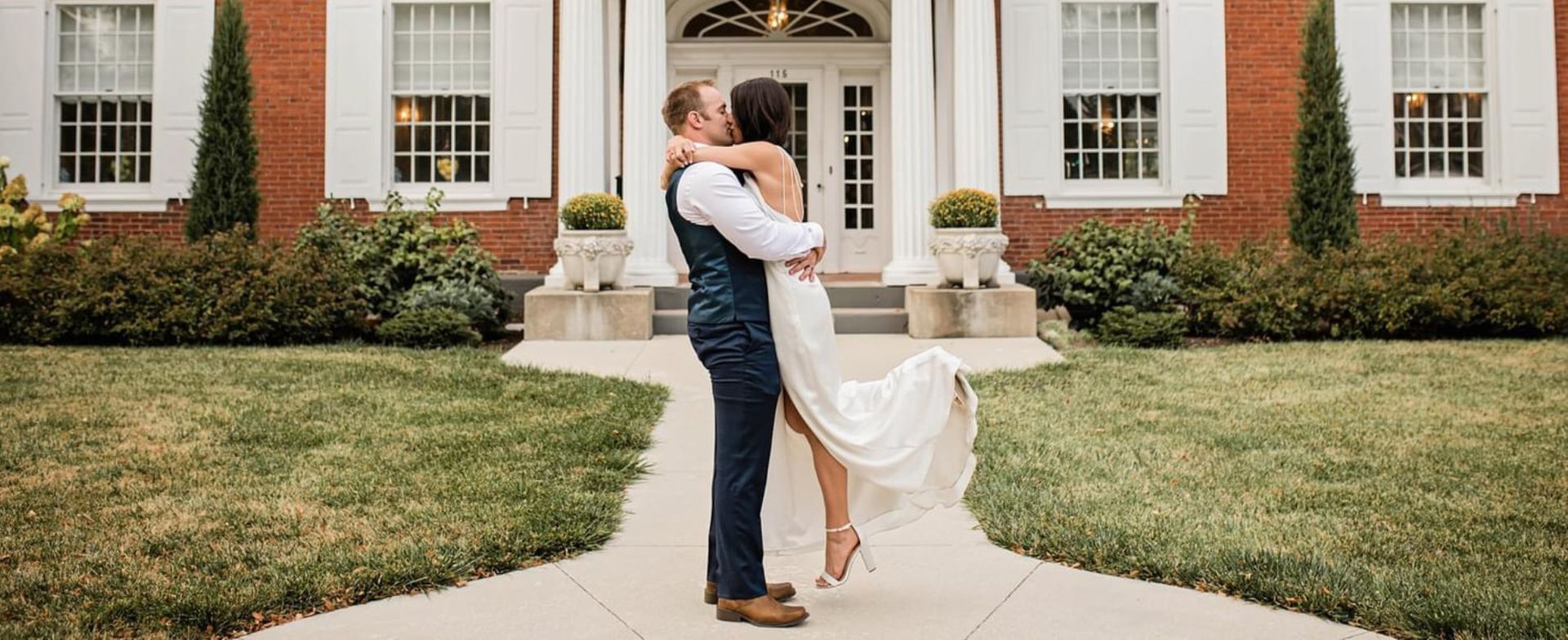 A bride and groom are standing in front of a large brick building.
