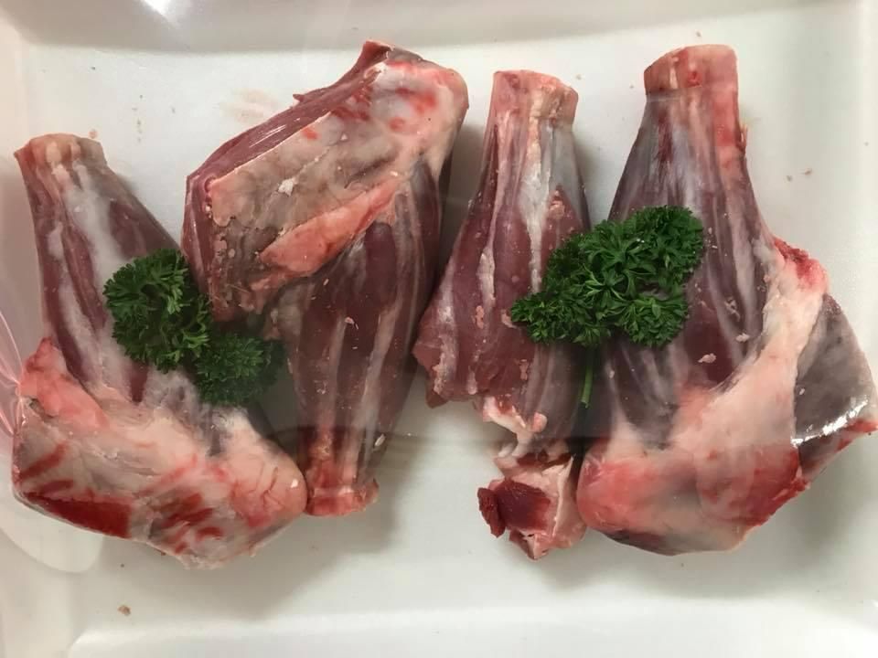 A White Plate Topped with Raw Lamb Shanks and Parsley — Holiday Coast Meat & Smallgoods in Glenn Innes, NSW