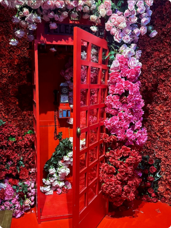 Red telephone booth adorned with pink and red flowers. The door is open, roses spilling out.