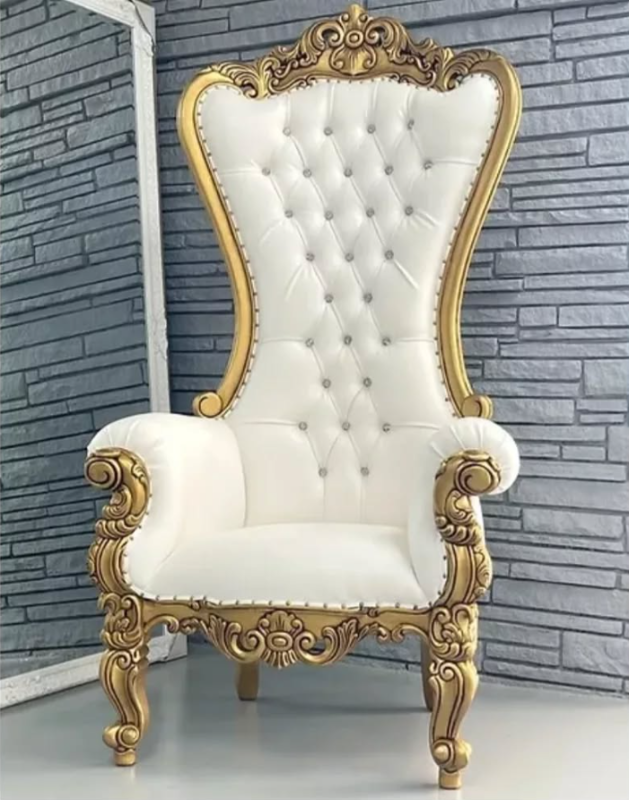 Ornate gold and white throne chair against a gray brick wall.