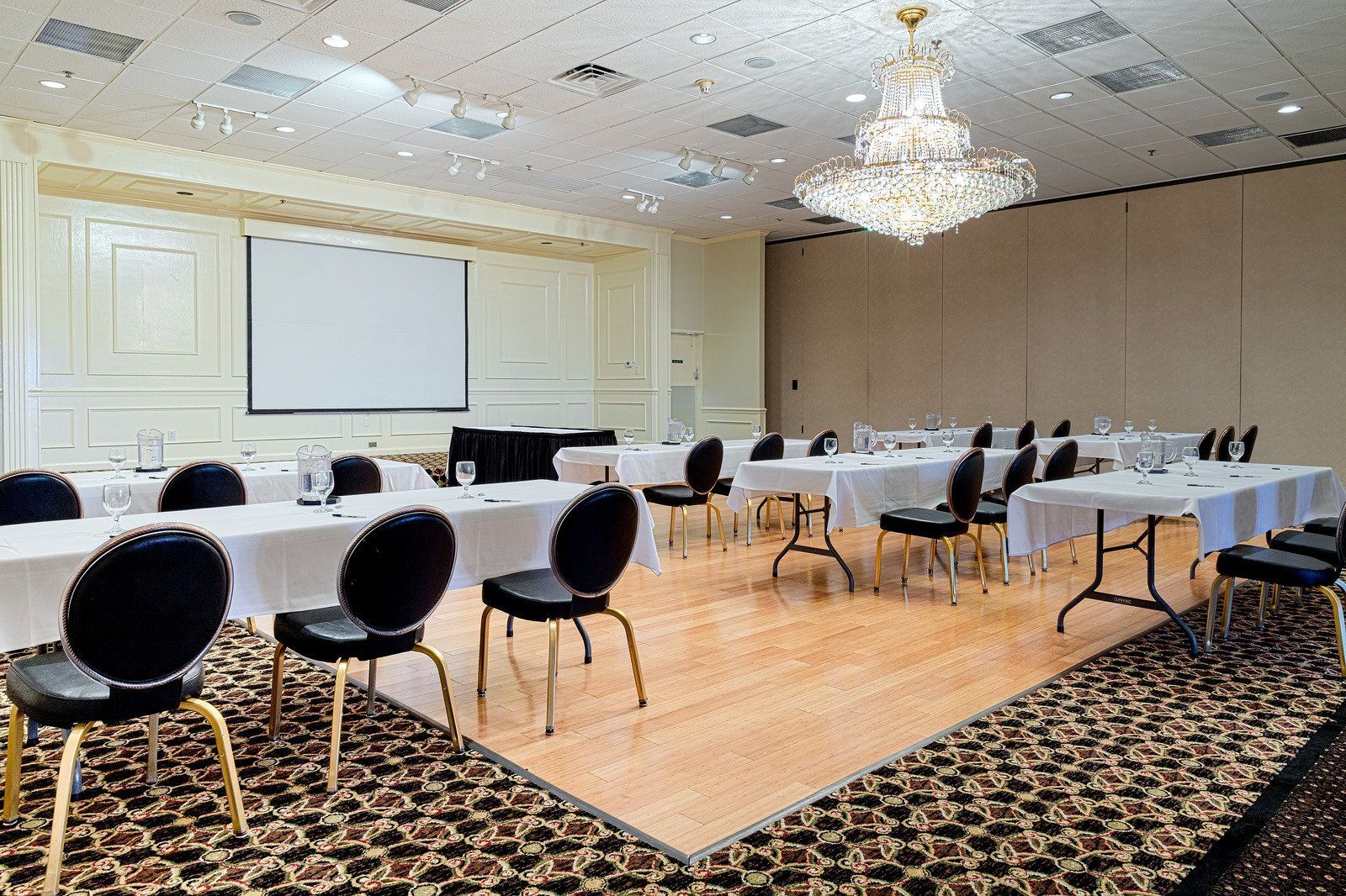 A conference room with tables, chairs, and a projection screen. A chandelier hangs from the ceiling.