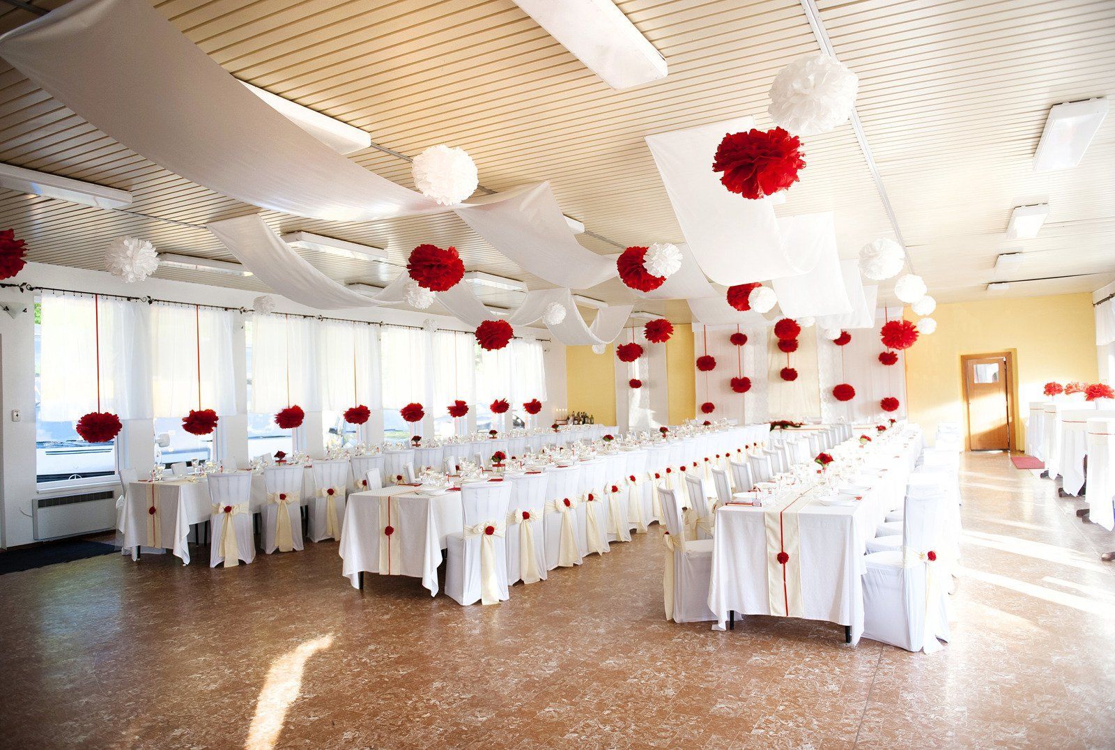 Formal dining room with long white tables, red and white decorations, and window light.