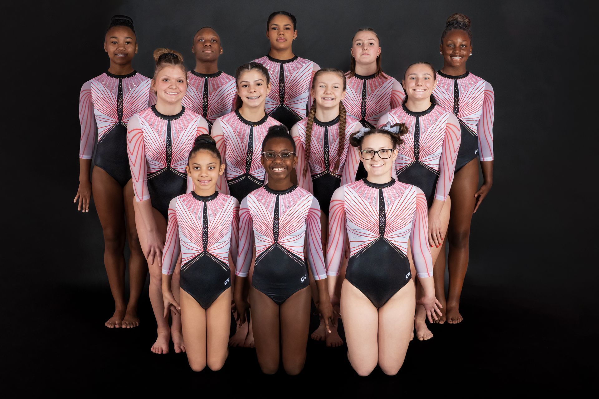 A group of young girls in pink and black leotards are posing for a picture.