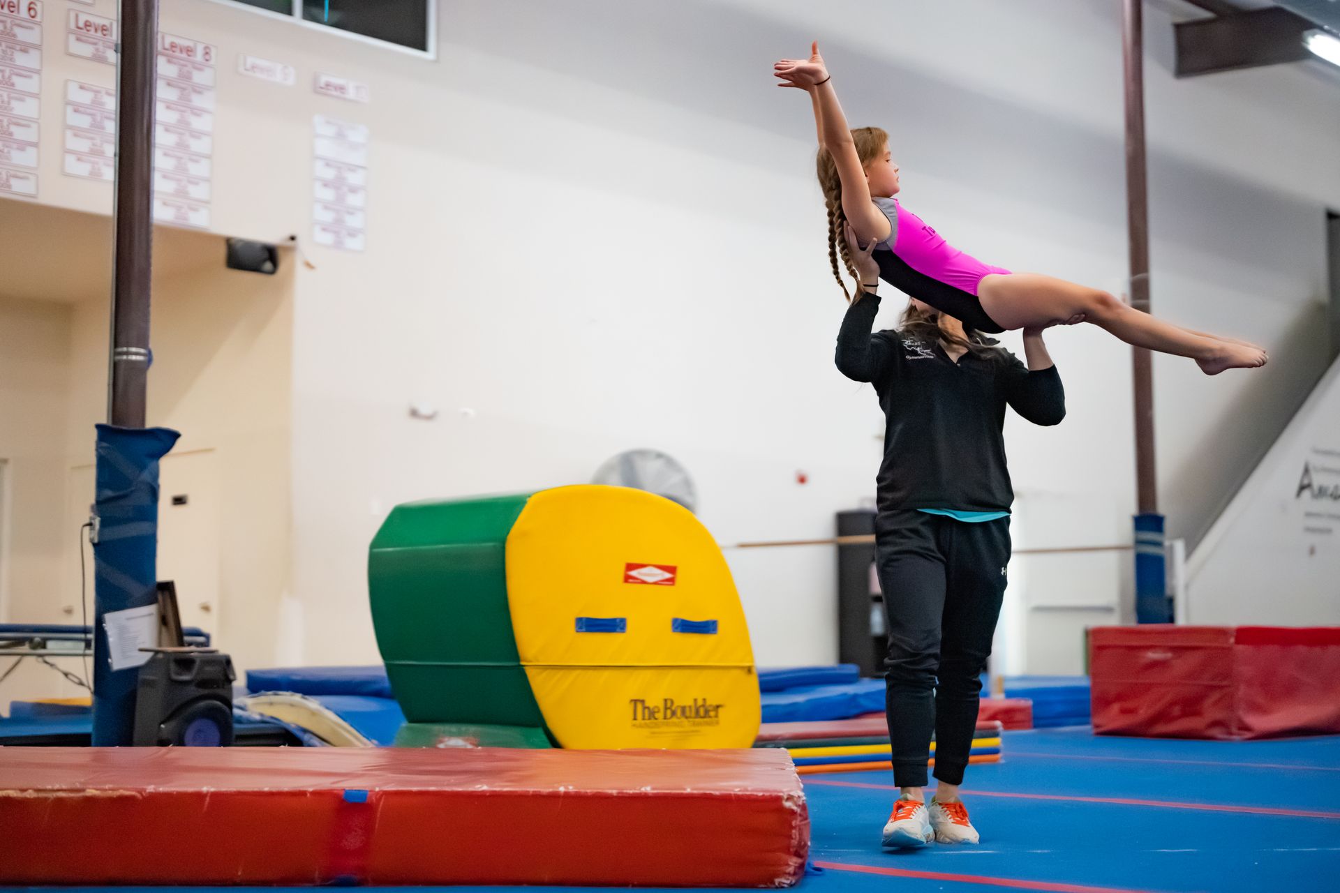 A man is carrying a girl on his shoulders in a gym.