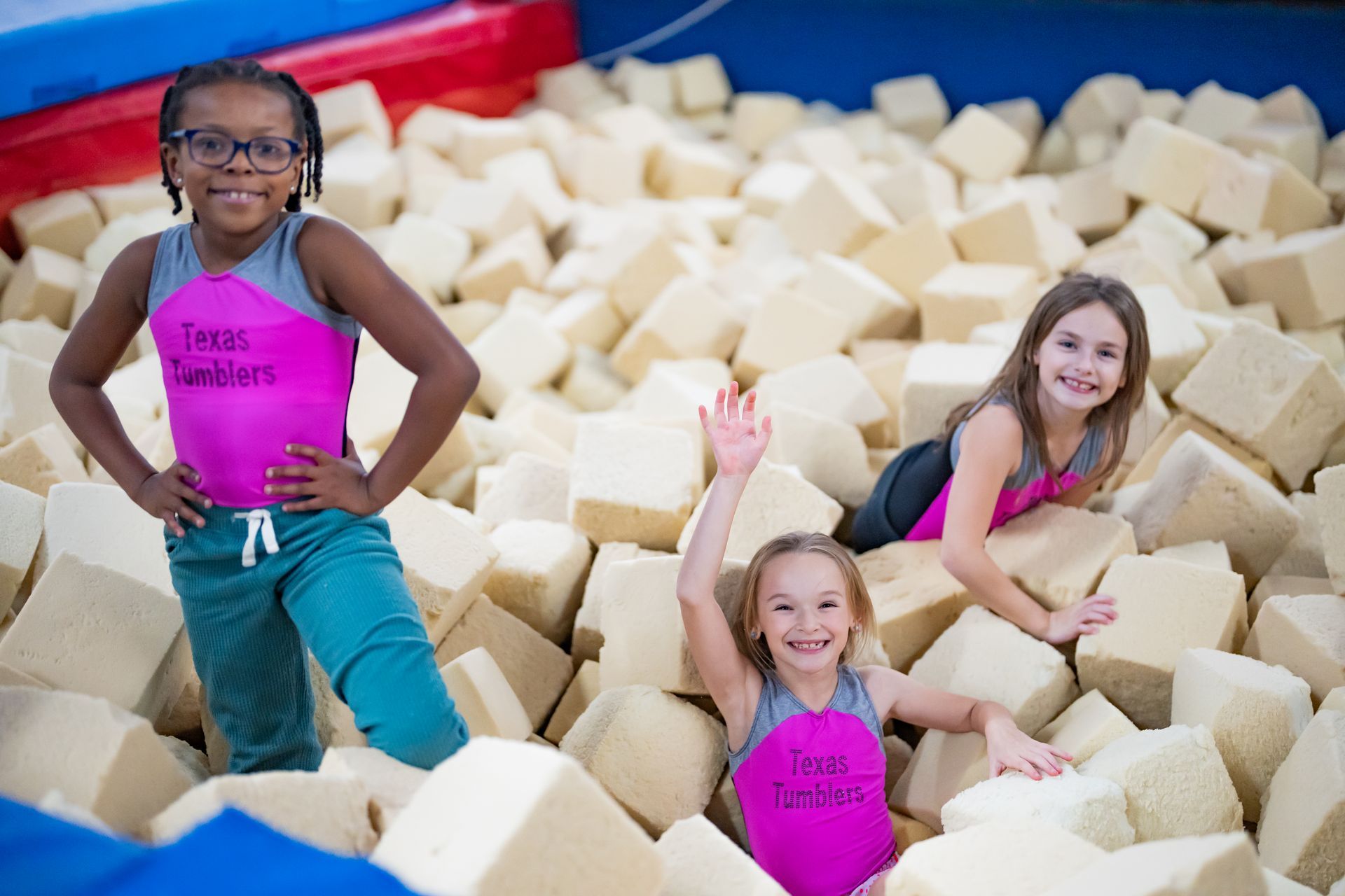 Three young girls are standing in a pile of foam cubes.