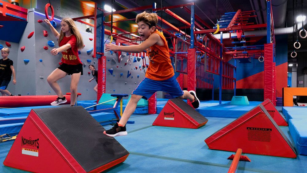 A boy and a girl are jumping over blocks in a gym.