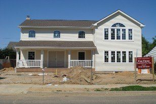 Two-story house under construction, with beige siding, porch, and unfinished landscaping.
