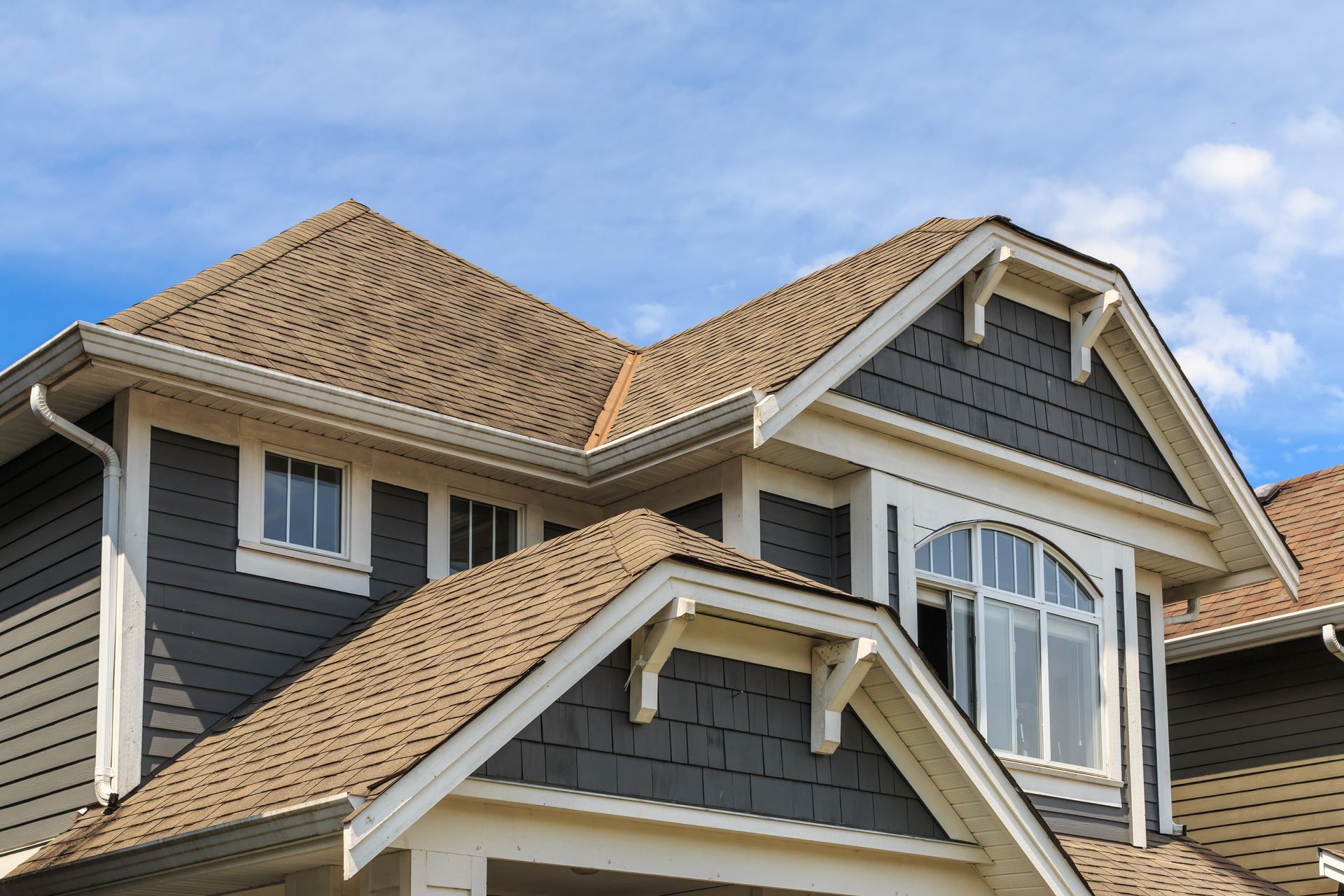House exterior with dark gray siding, tan roof, white trim, and a blue sky.