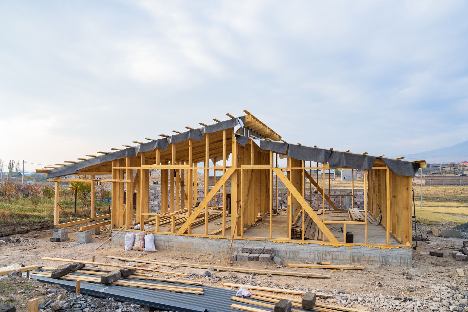Wooden house under construction; framework visible, construction materials on site, against a cloudy sky.