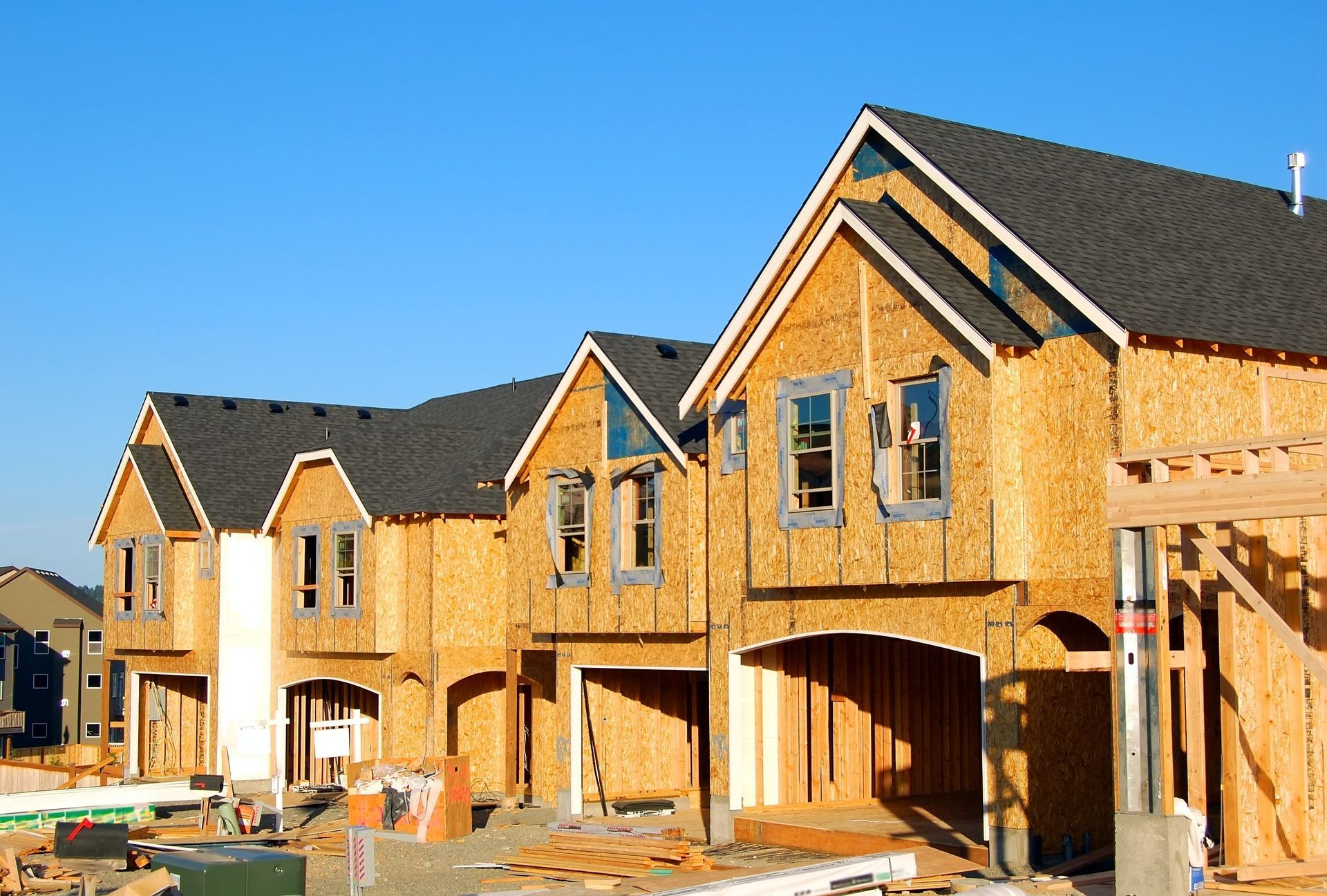 Row of houses under construction, wooden frames, blue sky.