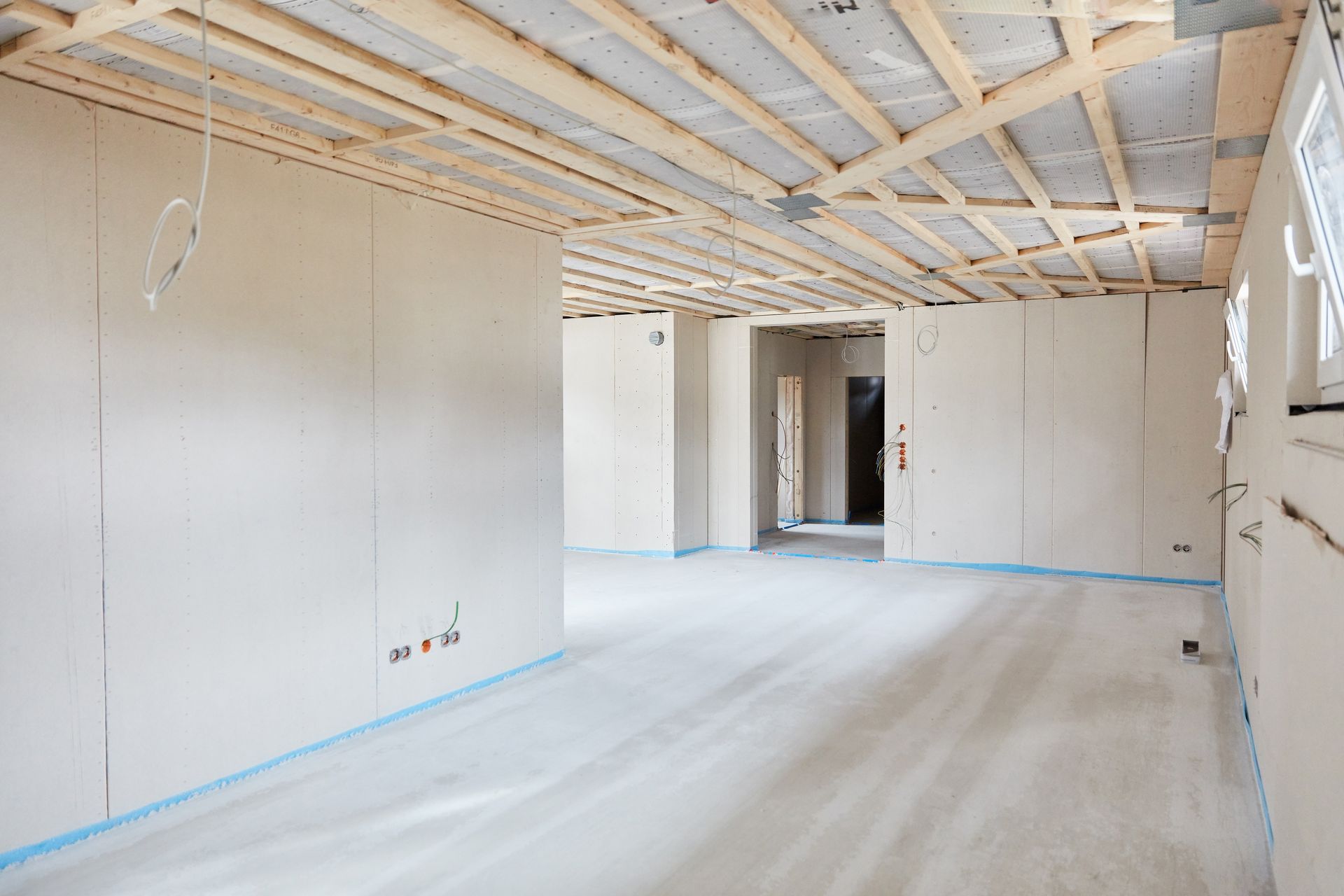 Interior of a room under construction, with exposed wooden beams, drywall, and unfinished floor.