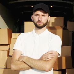 A man with his arms crossed is standing in front of a pile of cardboard boxes