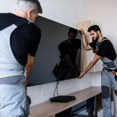 Two men are installing a flat screen tv on a wall.