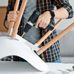 A man is using a drill to fix a chair