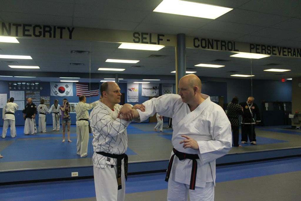 Two men are practicing martial arts in front of a wall that says integrity self control perseverance