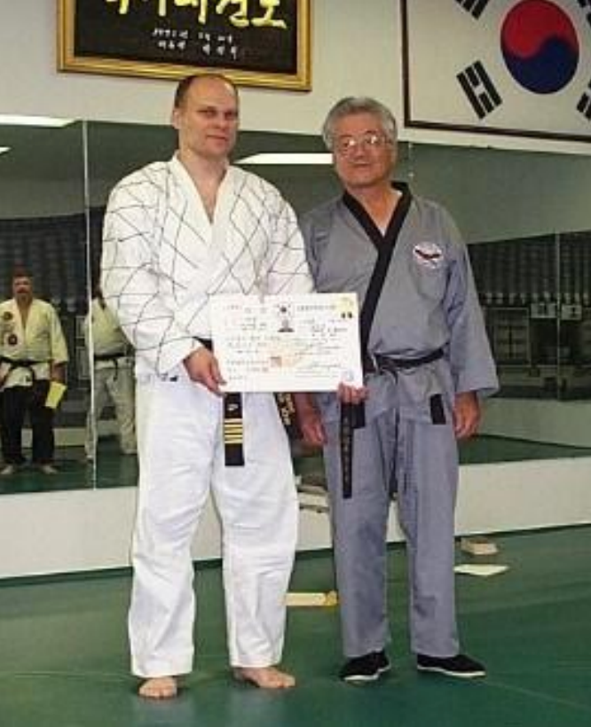 A man in a karate uniform is holding a certificate