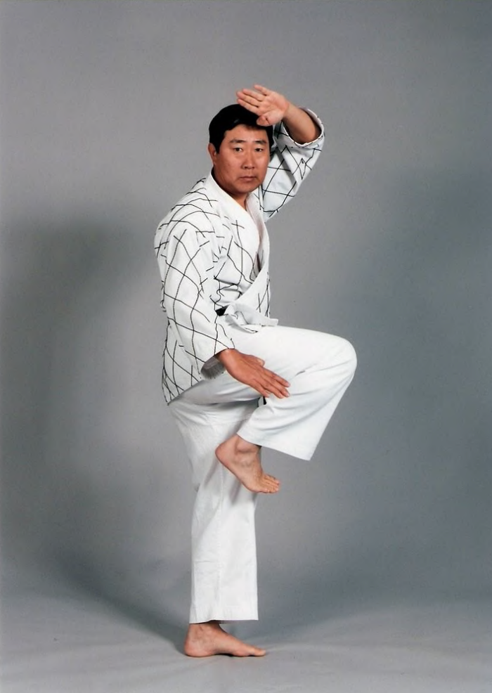A man in a karate uniform is standing on one leg.