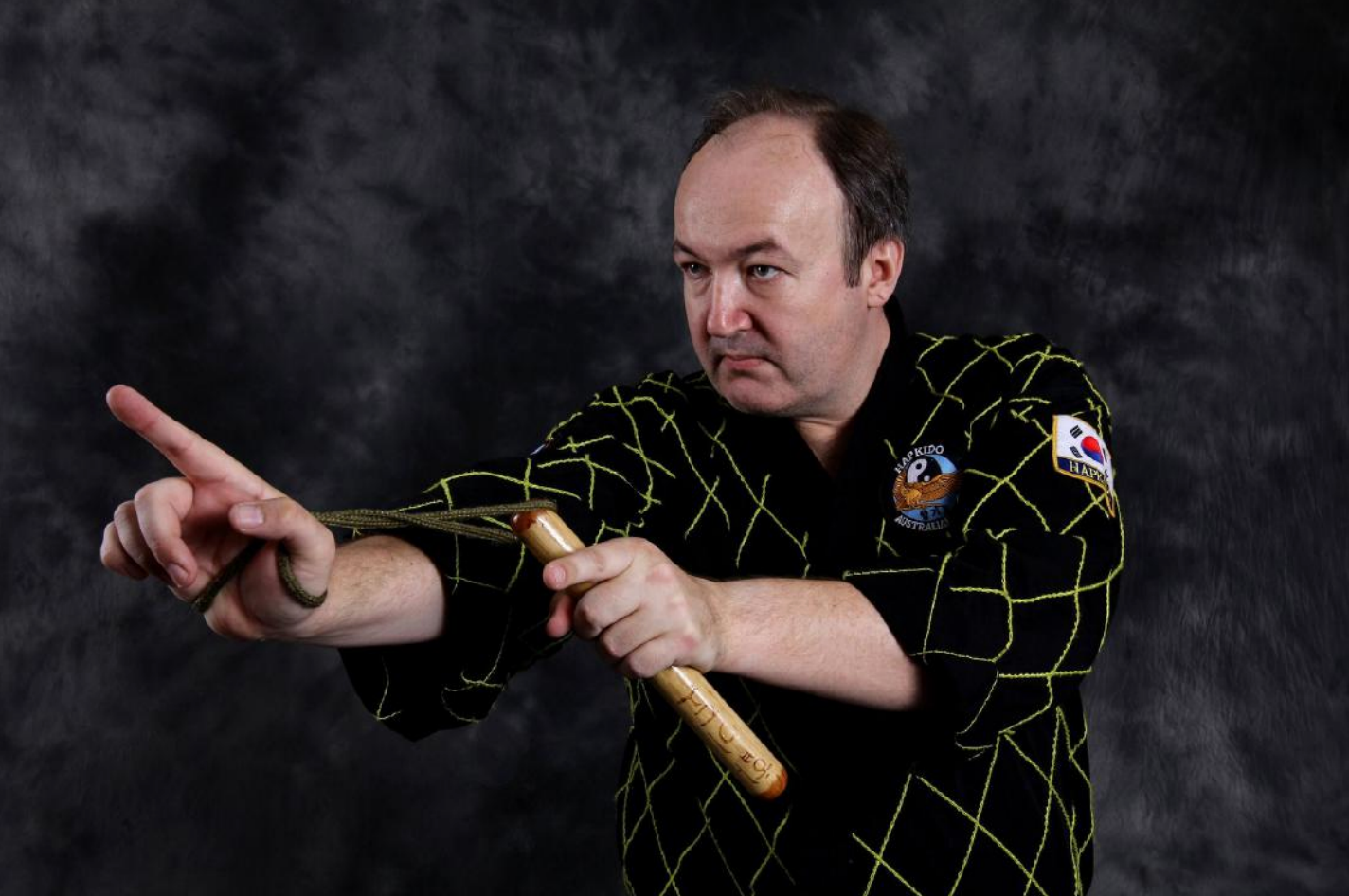 A man in a black and yellow shirt is holding a wooden stick and pointing.